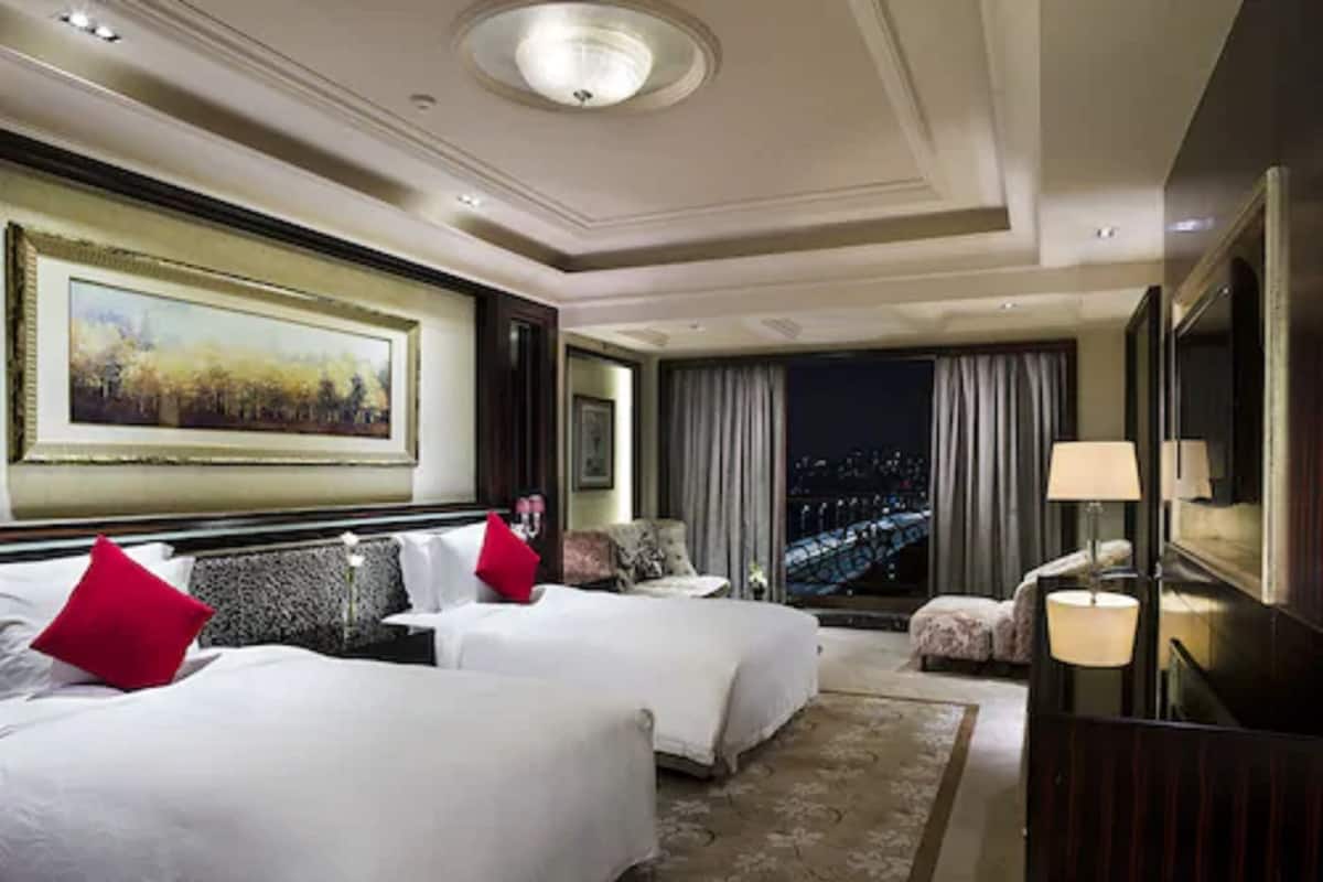 Une chambre d’hôtel avec deux lits, un grand tableau, une vue sur la ville et un lustre moderne.