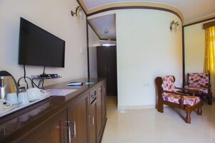 Una sala de estar con un televisor de pantalla plana montado en la pared, un mueble de madera con una bandeja de tazas blancas y un par de sillones estampados.