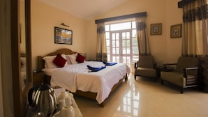 Quarto de hotel com cama, uma cadeira, cafeteira e janela com cortinas.
