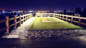 A nighttime view of a well-lit pathway leading to a building with a grassy area and a stone border. - After the Court Chiaohsi (Jiaoxi)