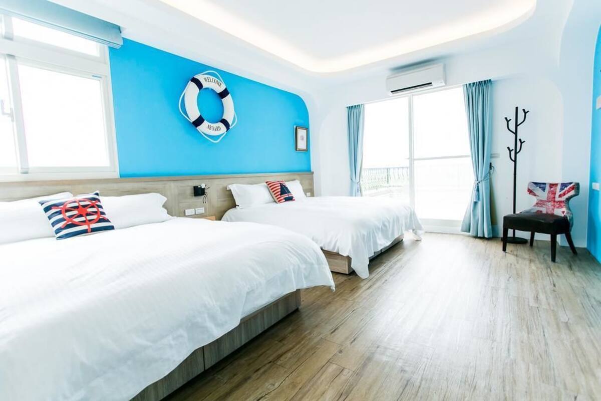 Een hotelkamer met twee bedden, een reddingsboei aan de muur, een kapstok en een raam met gordijnen.