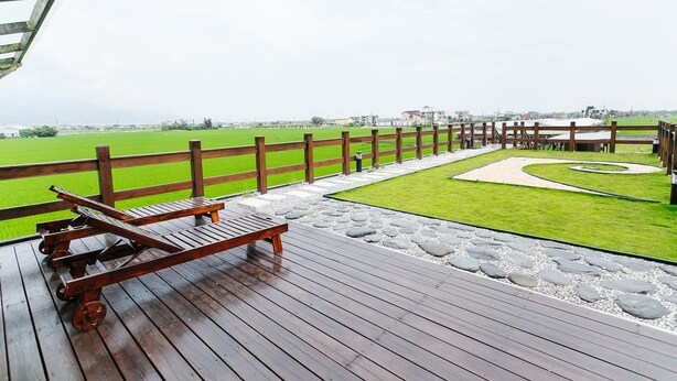 A wooden deck with a bench overlooking a green field and a paved area with a circular design. - After the Court Chiaohsi (Jiaoxi)