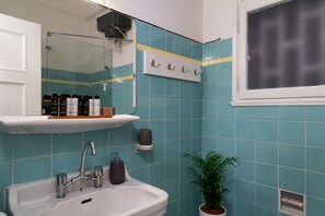 A bathroom with a white sink, a mirror, a shelf with toiletries, and a potted plant.