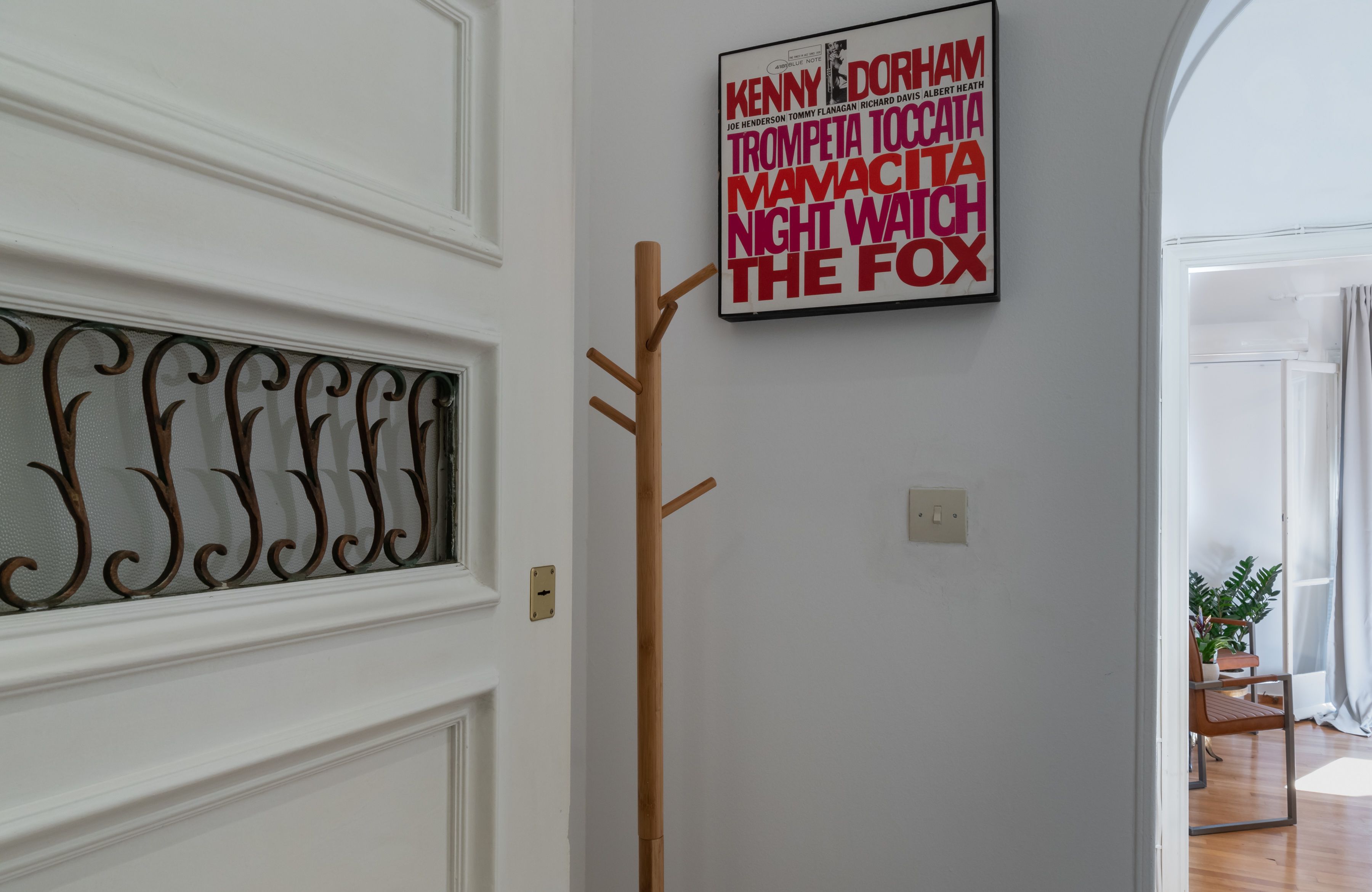 A hallway with a decorative metal grille, a wooden coat rack, and a framed sign with names.