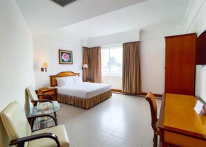 A hotel room with a bed, a desk, a chair, a lamp, and a window with curtains. - Asia Palace Hotel (Phnom Penh)
