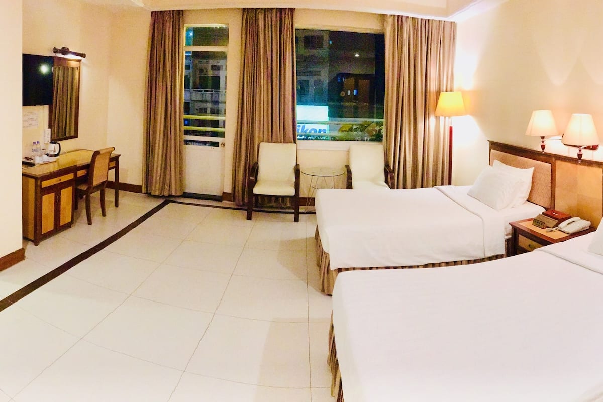 A hotel room with two beds, a desk with a chair, a TV, and a window with curtains.