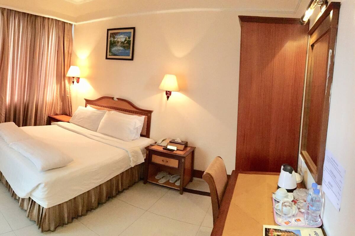 A hotel room with a large bed, two bedside lamps, a wooden nightstand, a chair, a desk, and a mirror.