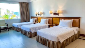 A hotel room with two beds, a chair, a window with curtains, and a view of buildings and palm trees. - Asia Palace Hotel (Phnom Penh)