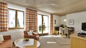 A cozy living room with a sofa, a round table with a bowl of fruit, and a dining area with a table and chairs. - Ferienwohnungen Wölfl (Bodenmais)