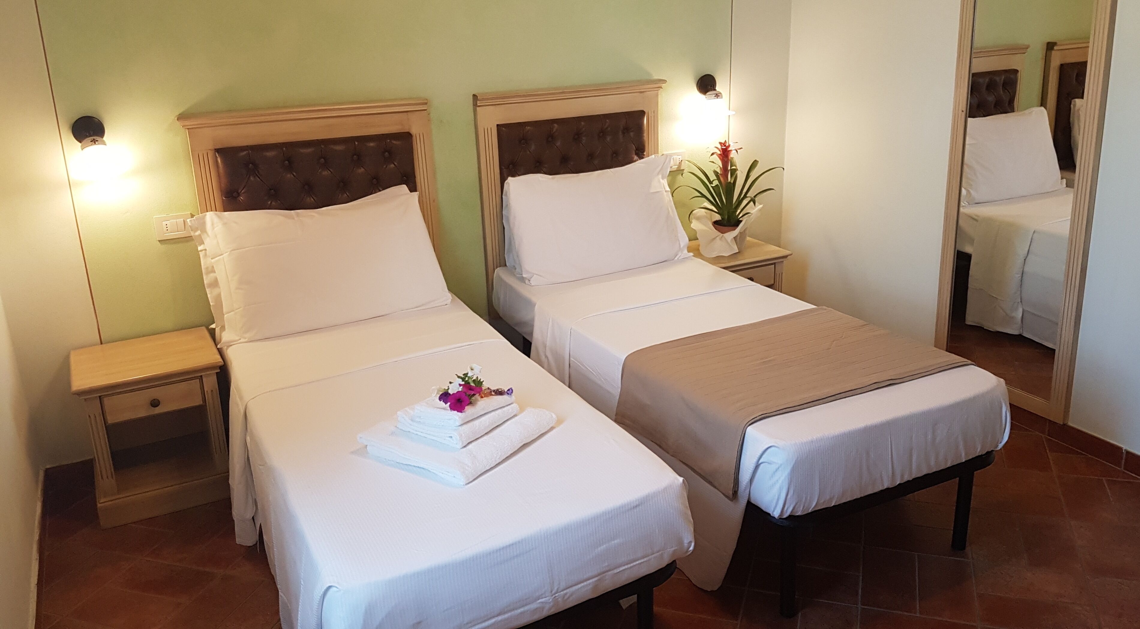 A hotel room with two beds, each with a headboard, bedside tables, and a mirror.