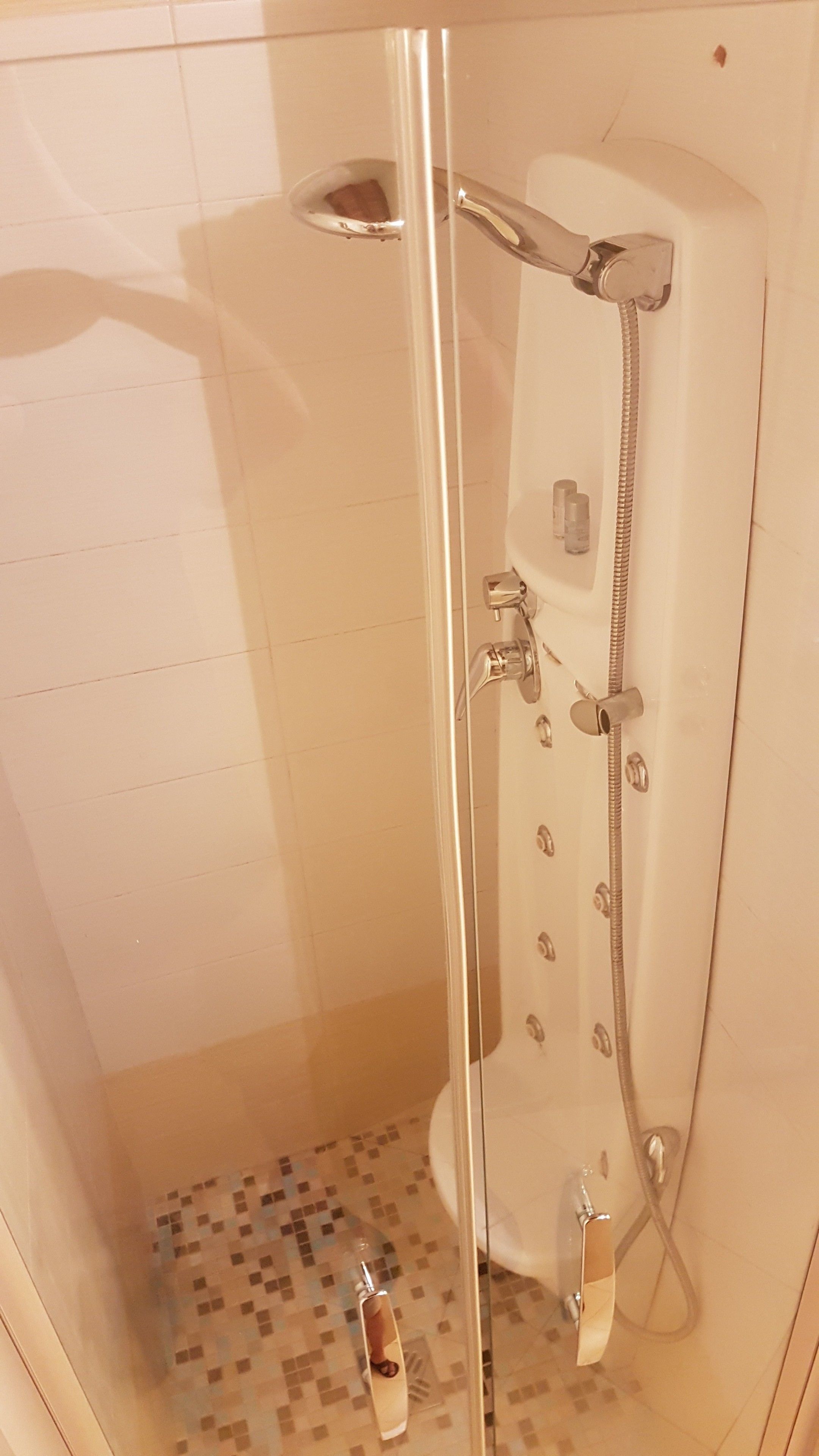 Cabina de ducha con paredes de vidrio, un cabezal de ducha manual y un grifo instalado en la pared.