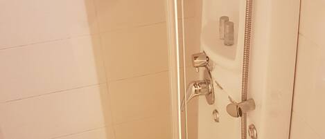 Cabina de ducha con paredes de vidrio, un cabezal de ducha manual y un grifo instalado en la pared.