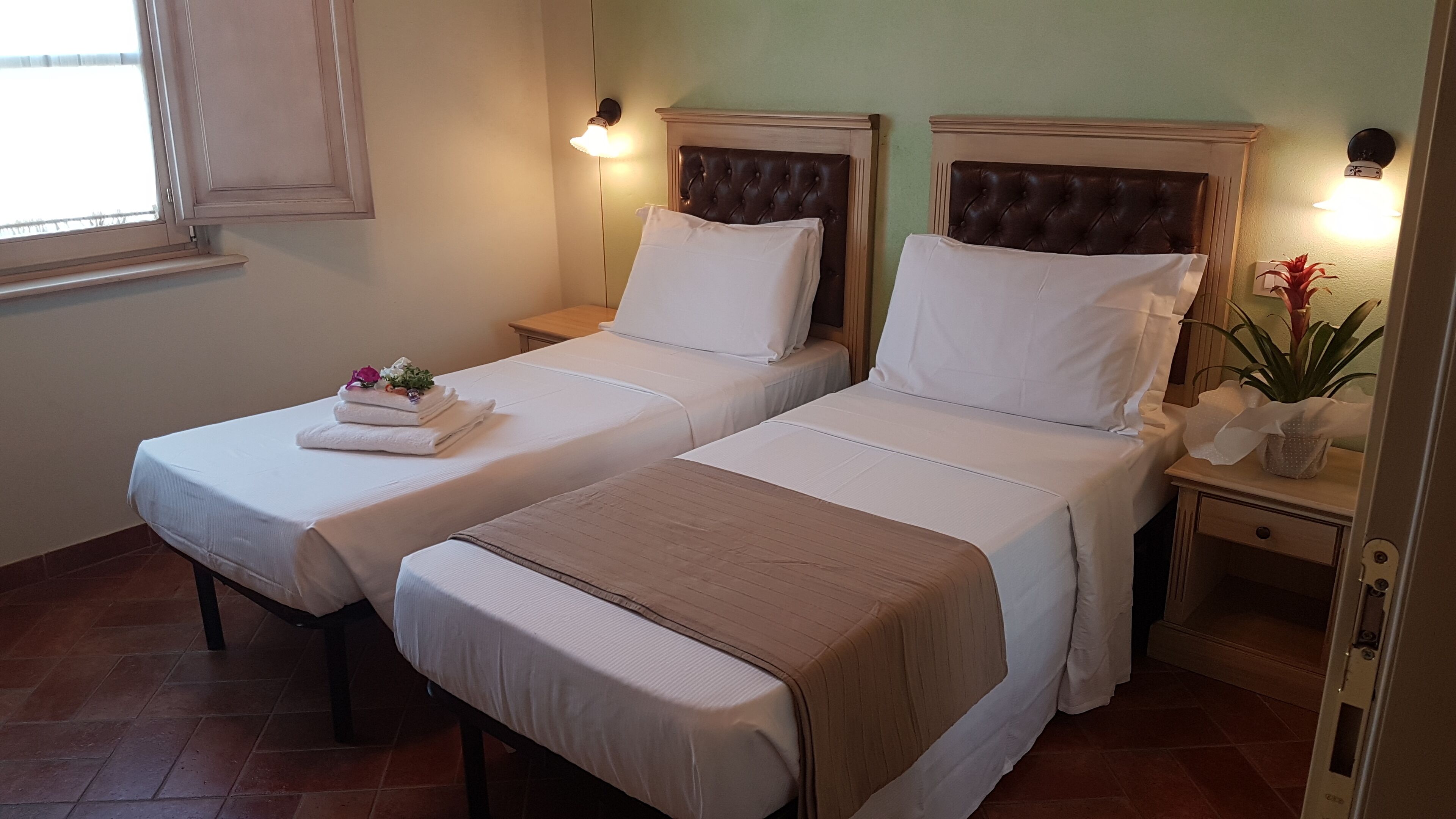 A hotel room with two beds, each with a headboard, bedside tables, and a window.