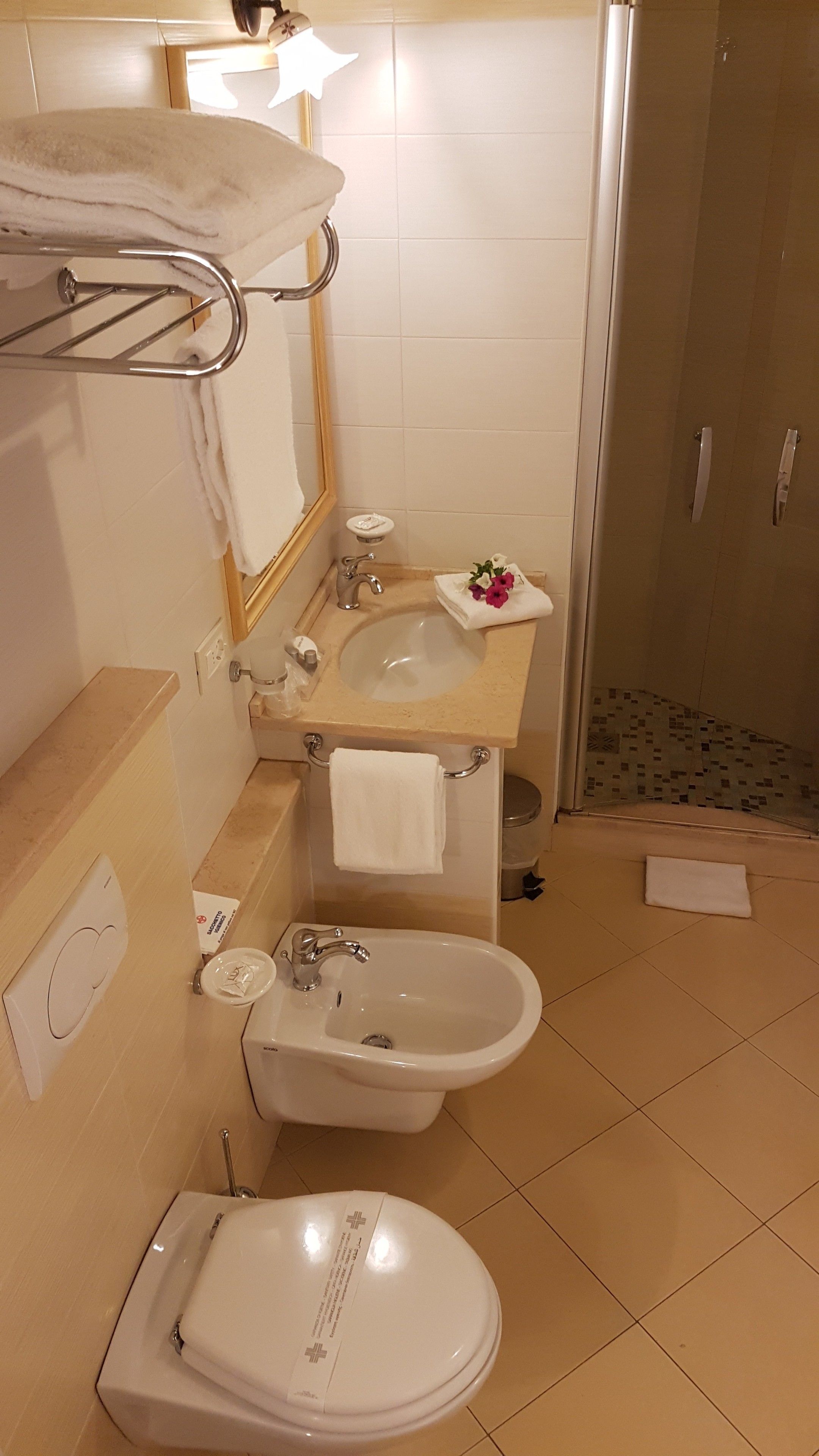 A bathroom with a sink, bidet, and toilet. There is a towel rack above the sink and a mirror on the wall.