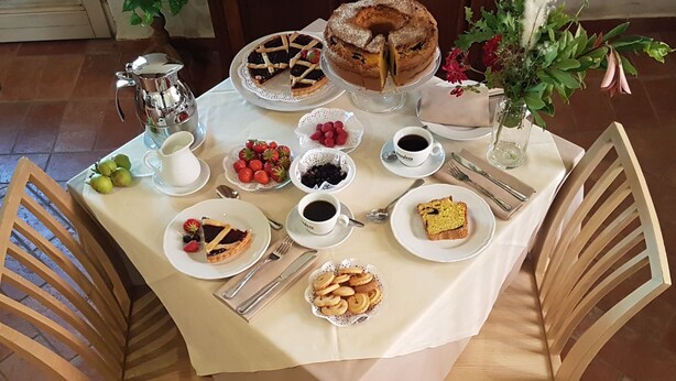 Een eettafel gedekt met verschillende desserts, koffie en gebak, omringd door houten stoelen.