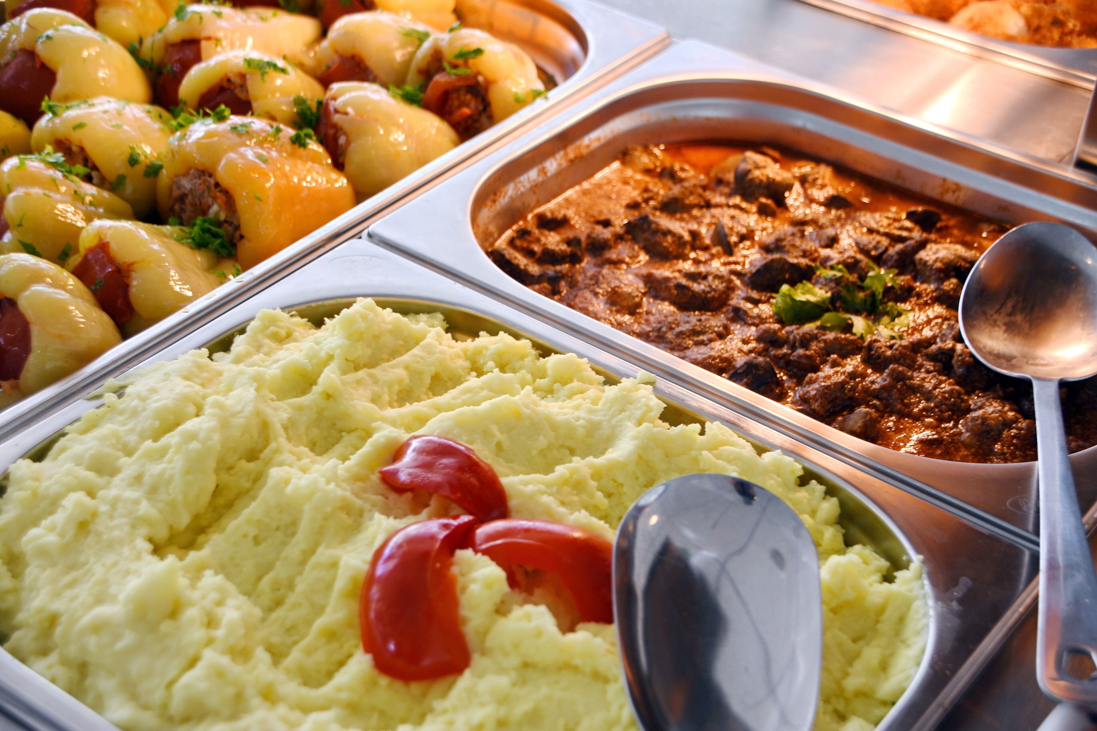 A buffet with various dishes including mashed potatoes, meat stew, and stuffed peppers.