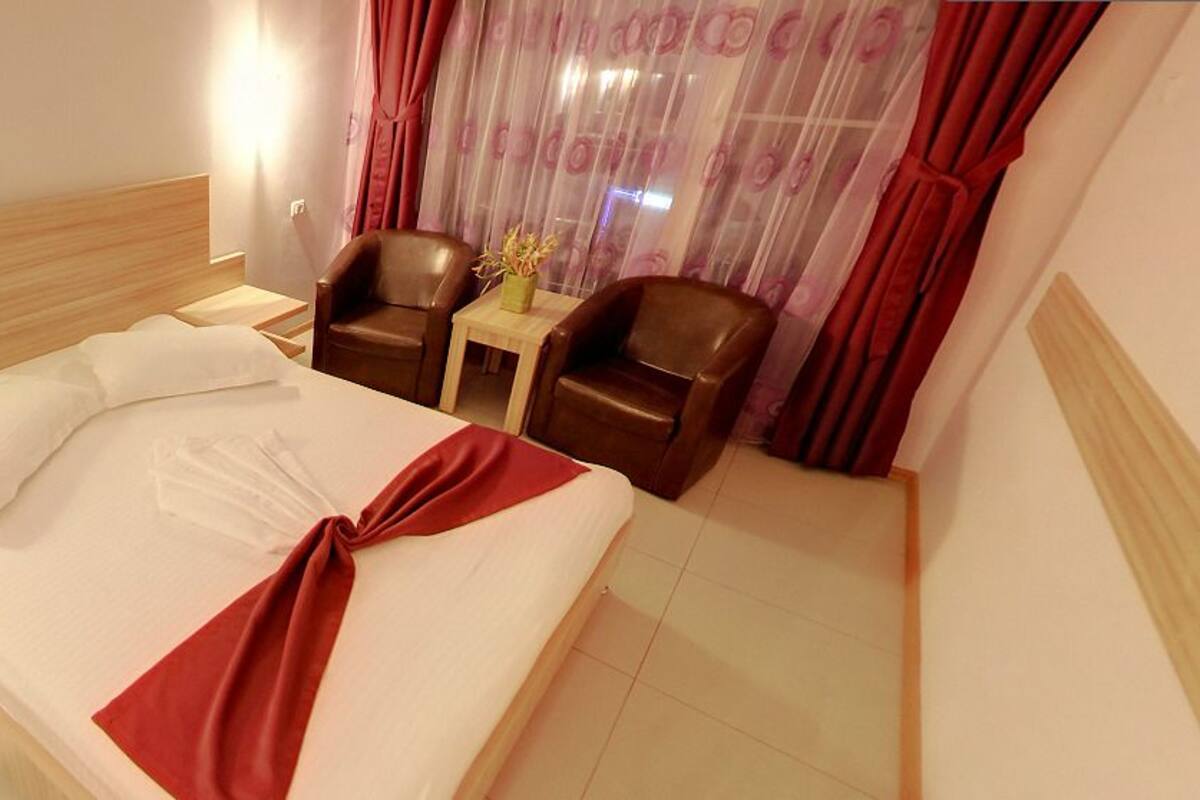 A hotel room with a bed, two chairs, a small table, and a nightstand.