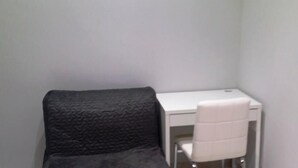 A small, compact room with a white desk and chair, a dark textured blanket draped over the chair, and a plain wall. - B&B La Ferrovia (Benevento)