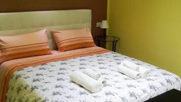 A bed with a floral bedspread, two pillows, and two rolled towels.
