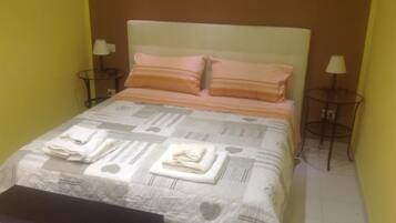 A neatly made bed with a patterned bedspread, pillows, and folded towels on a bedside table.