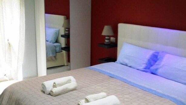 A hotel room with a bed, a nightstand, a lamp, and a chair in the background. - B&B La Ferrovia (Benevento)