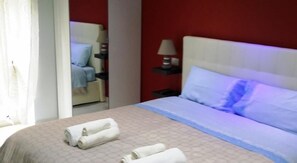 A hotel room with a bed, a nightstand, a lamp, and a chair in the background. - B&B La Ferrovia (Benevento)