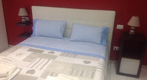A bedroom with a bed, two pillows, a bedside table with a lamp, and a nightstand with a lamp. - B&B La Ferrovia (Benevento)