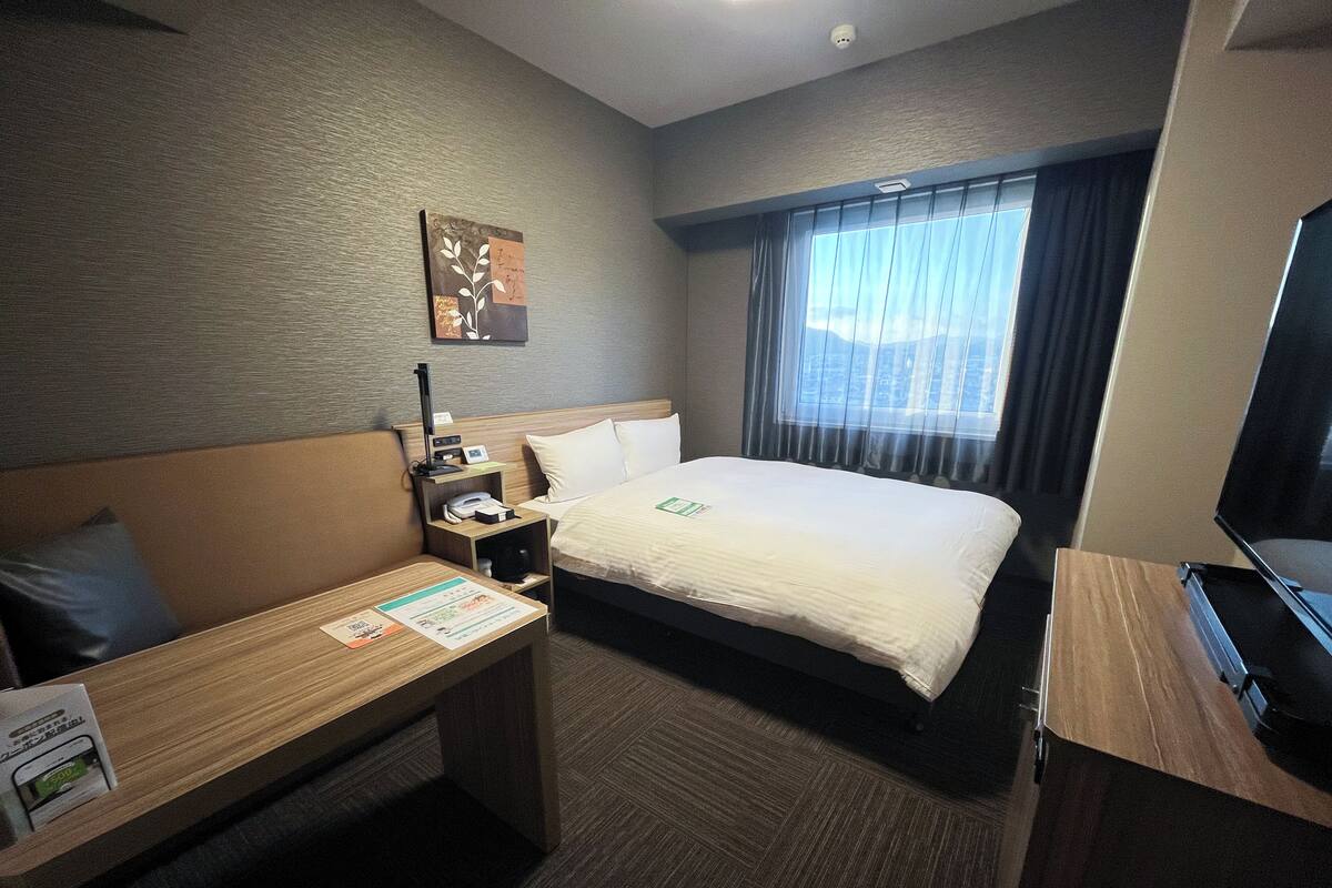 Een hotelkamer met een bed, bureau, stoel, televisie en een raam met gordijnen.