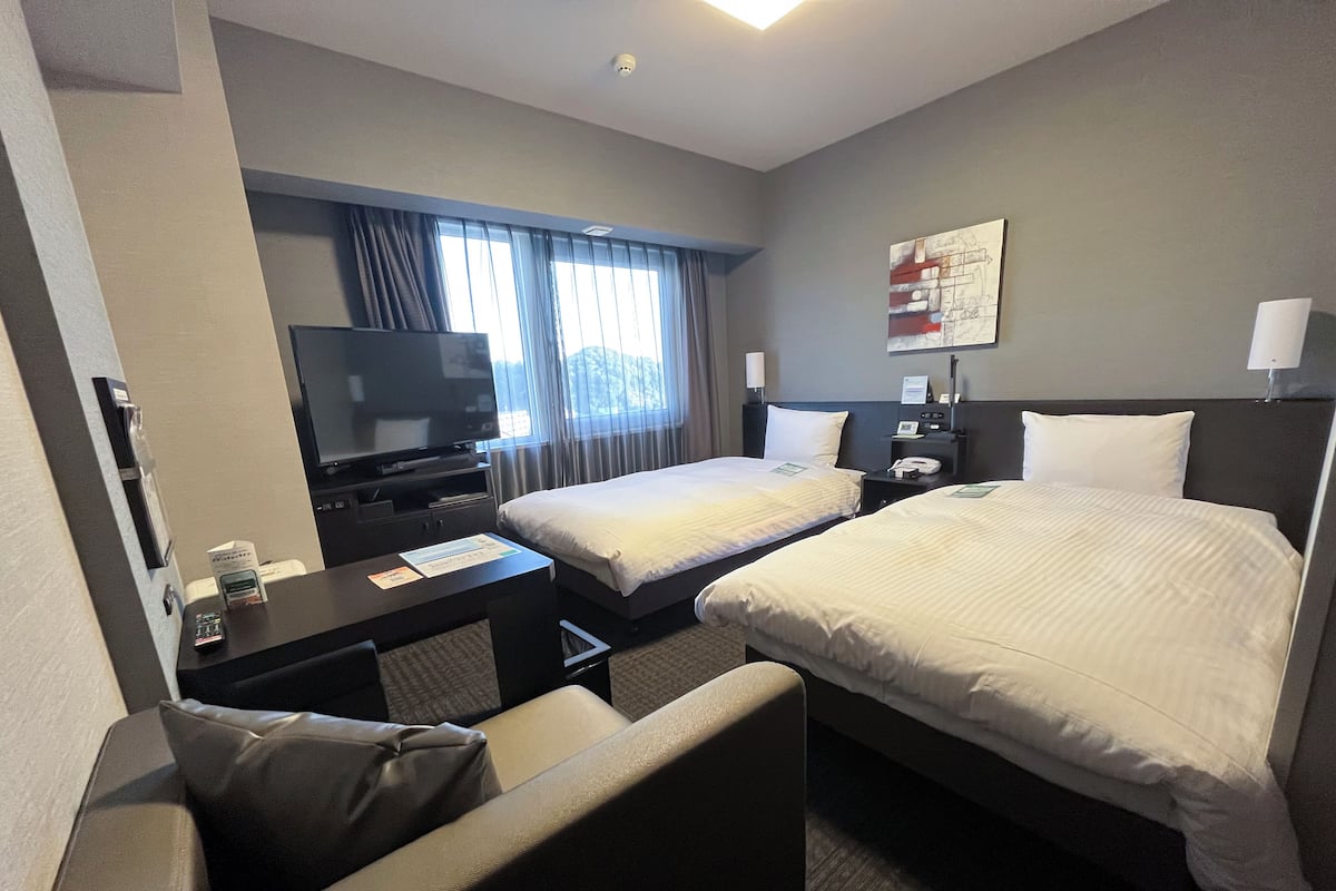 Hotelkamer met twee bedden, een bureau met televisie, een stoel en een raam met gordijnen.