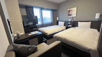 A hotel room with two beds, a desk with a TV, a chair, and a window with curtains.