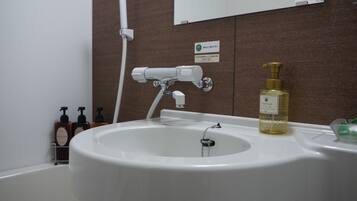 A bathroom with a white sink, a handheld showerhead, and a bottle of foam soap.