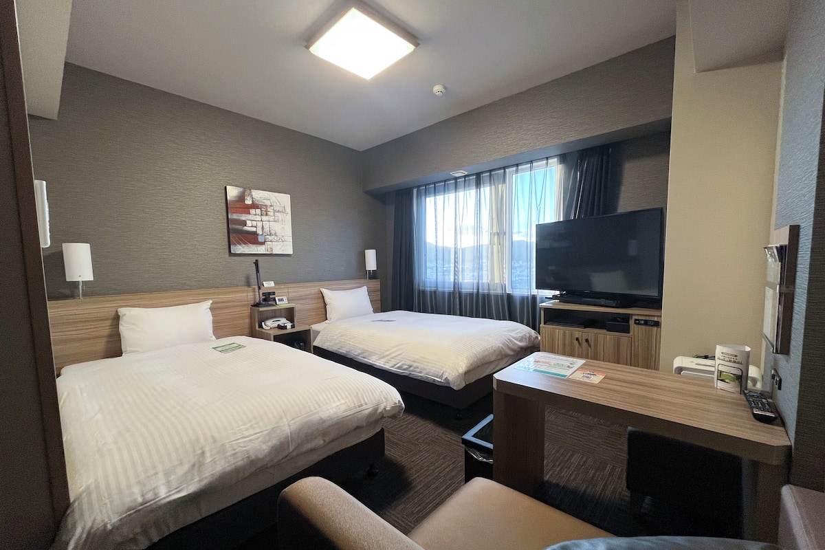 Een hotelkamer met twee bedden, een bureau, een televisie en een raam met gordijnen.