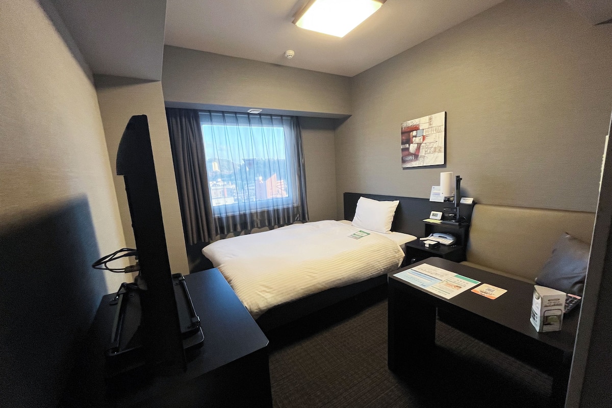 Een hotelkamer met een bed, bureau, stoel, televisie en raam met gordijnen.