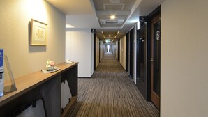 A hotel hallway with a reception desk, framed artwork, and doors leading to guest rooms.