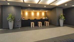 A reception area with a dark-colored reception desk, three wooden stools, and two large potted plants.