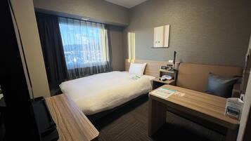 A hotel room with a bed, bedside table, and a desk with a chair.