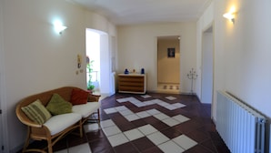 Una sala con piso a cuadros, un sofá con cojines, un radiador y un pasillo que conduce a otra habitación.