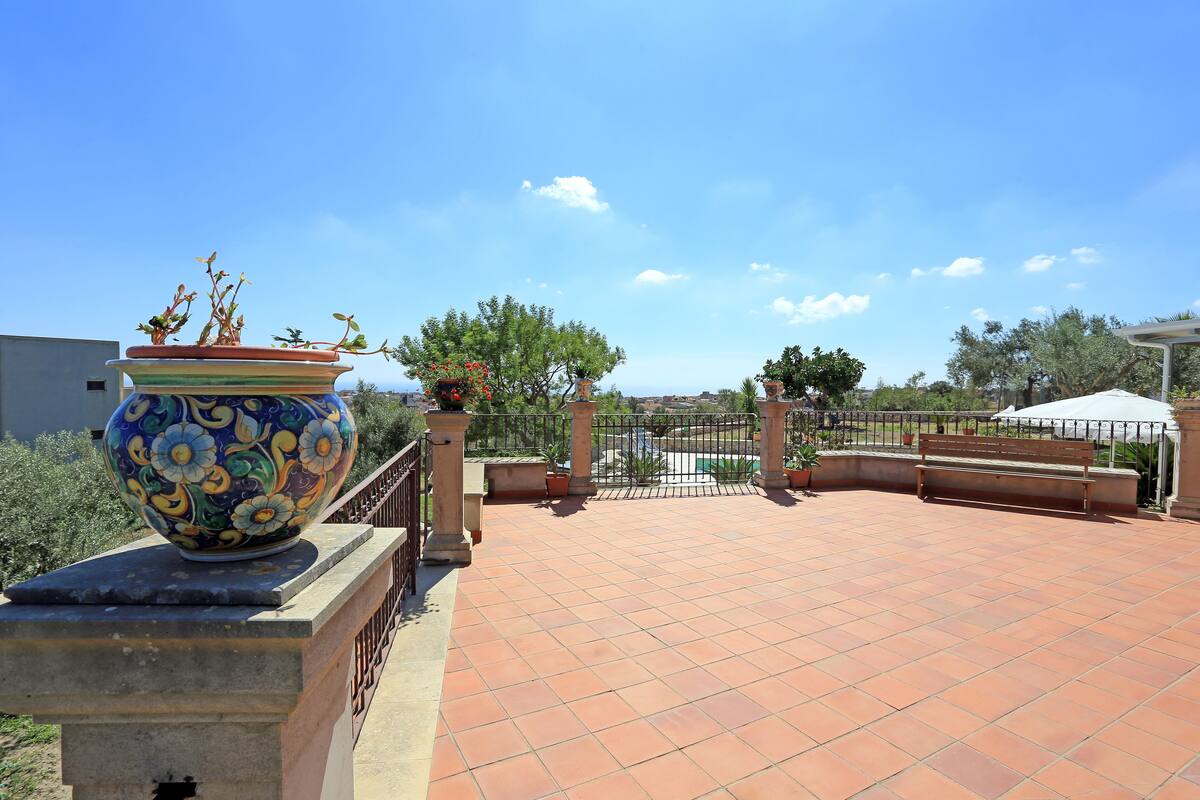 Una terraza en la azotea con tejas de terracota, una maceta de cerámica decorativa y una verja de metal.