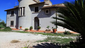 Un edificio de dos pisos con una torre curva, una entrada porticada y plantas en macetas alrededor de la propiedad.