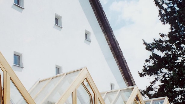A building with large glass windows and wooden frames, surrounded by a cobblestone path and greenery. - Seehotel am Neuklostersee (Zurow)