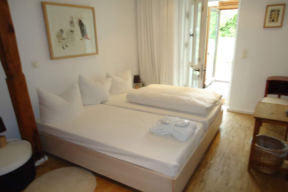 Una cama doble con sábanas blancas, una mesita de noche con lámpara y un cuadro en la pared.