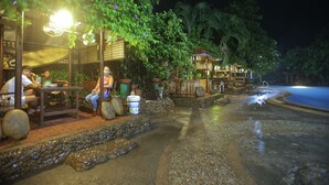An outdoor restaurant with tables and chairs, surrounded by greenery and a water feature. - Villa Elita (Sudipen)