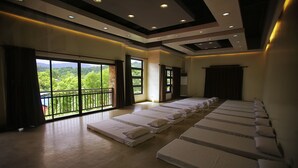 A room with multiple beds arranged in rows, large windows with curtains, and a view of greenery outside. - Villa Elita (Sudipen)