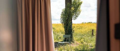 A bedroom with a bed, curtains, and a window view of a tree and field.