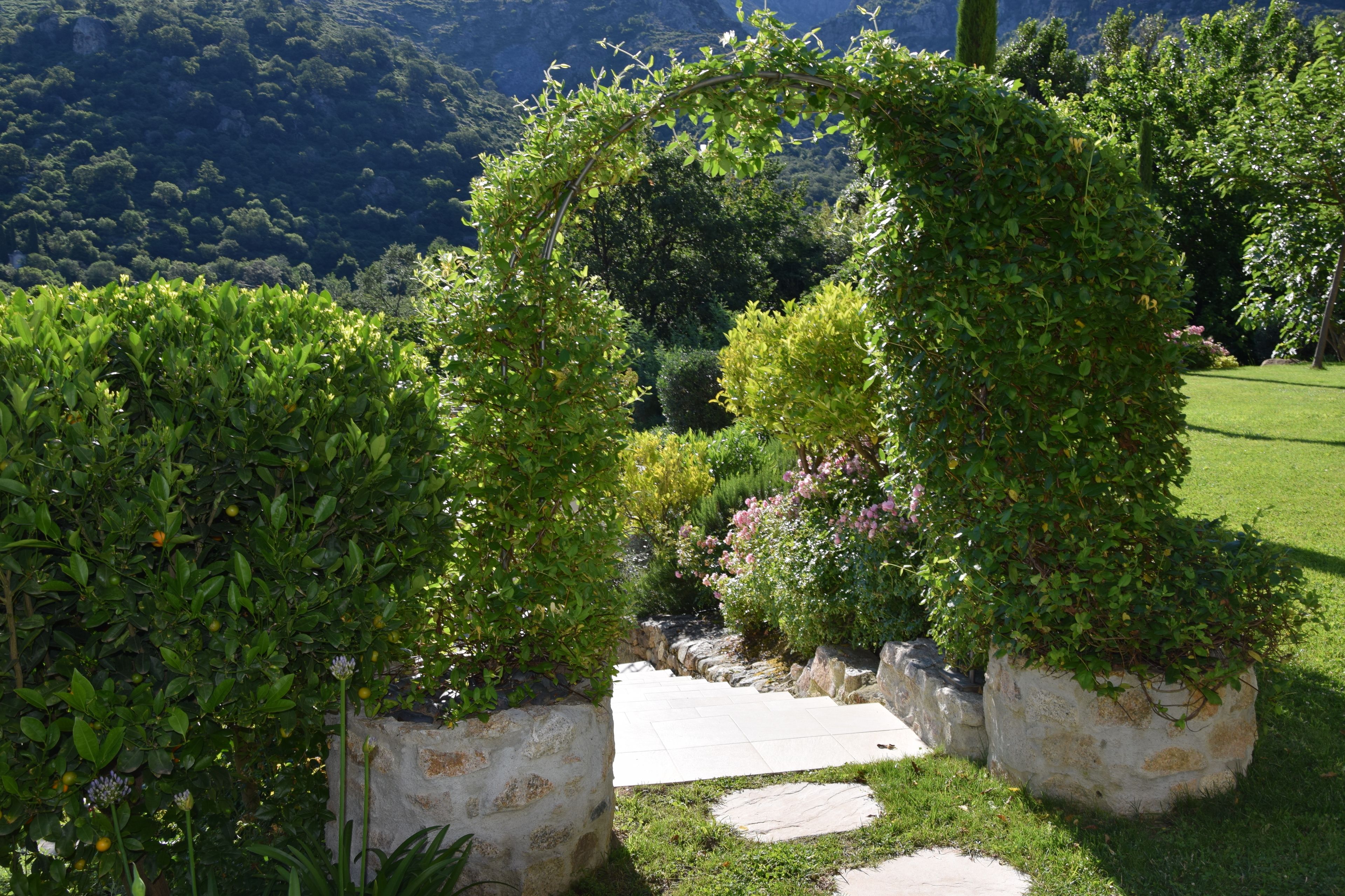 A garden with a stone pathway leading to a circular archway surrounded by lush greenery.
