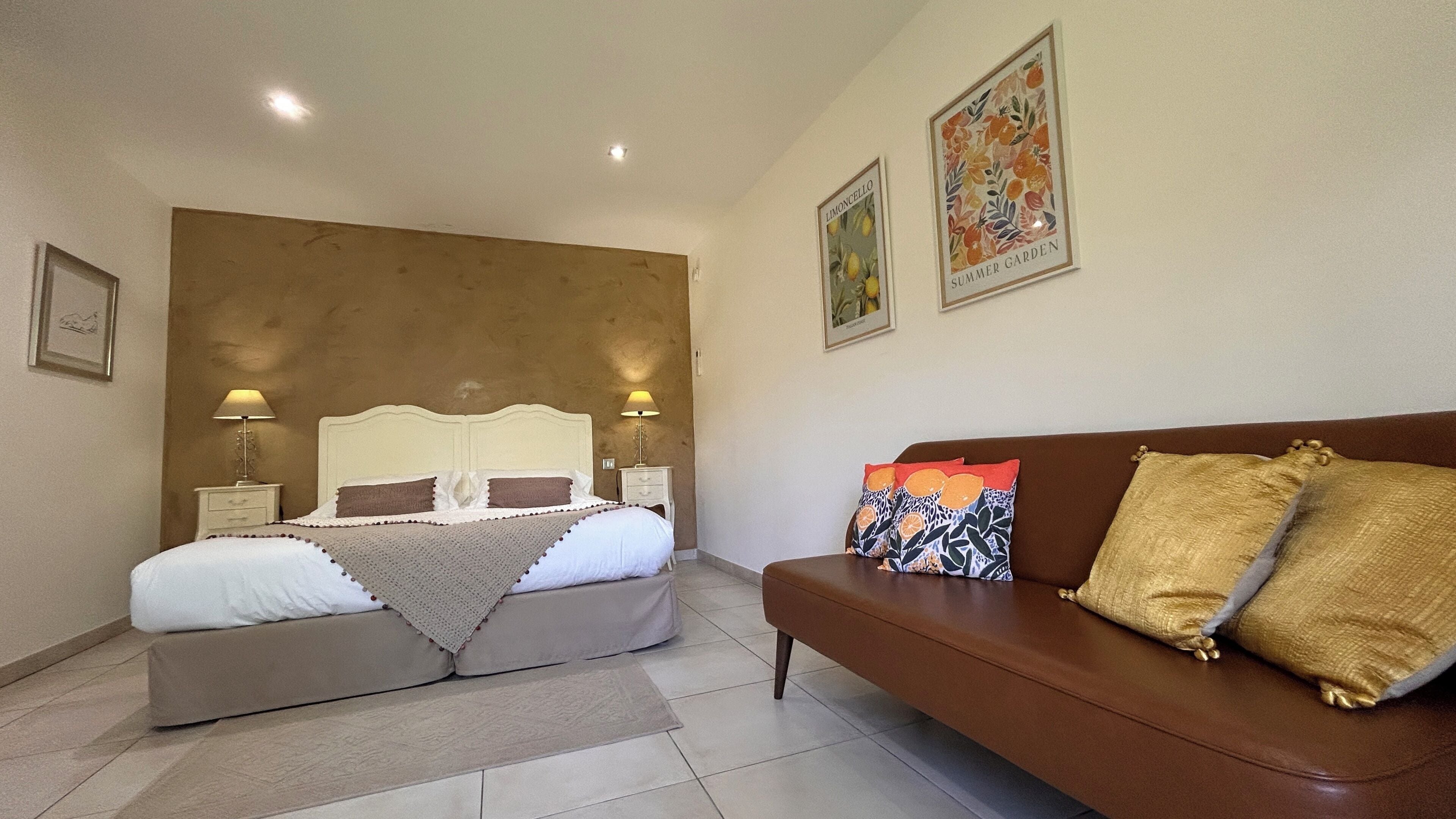 A bedroom with a double bed, a brown sofa, and two bedside tables with lamps.