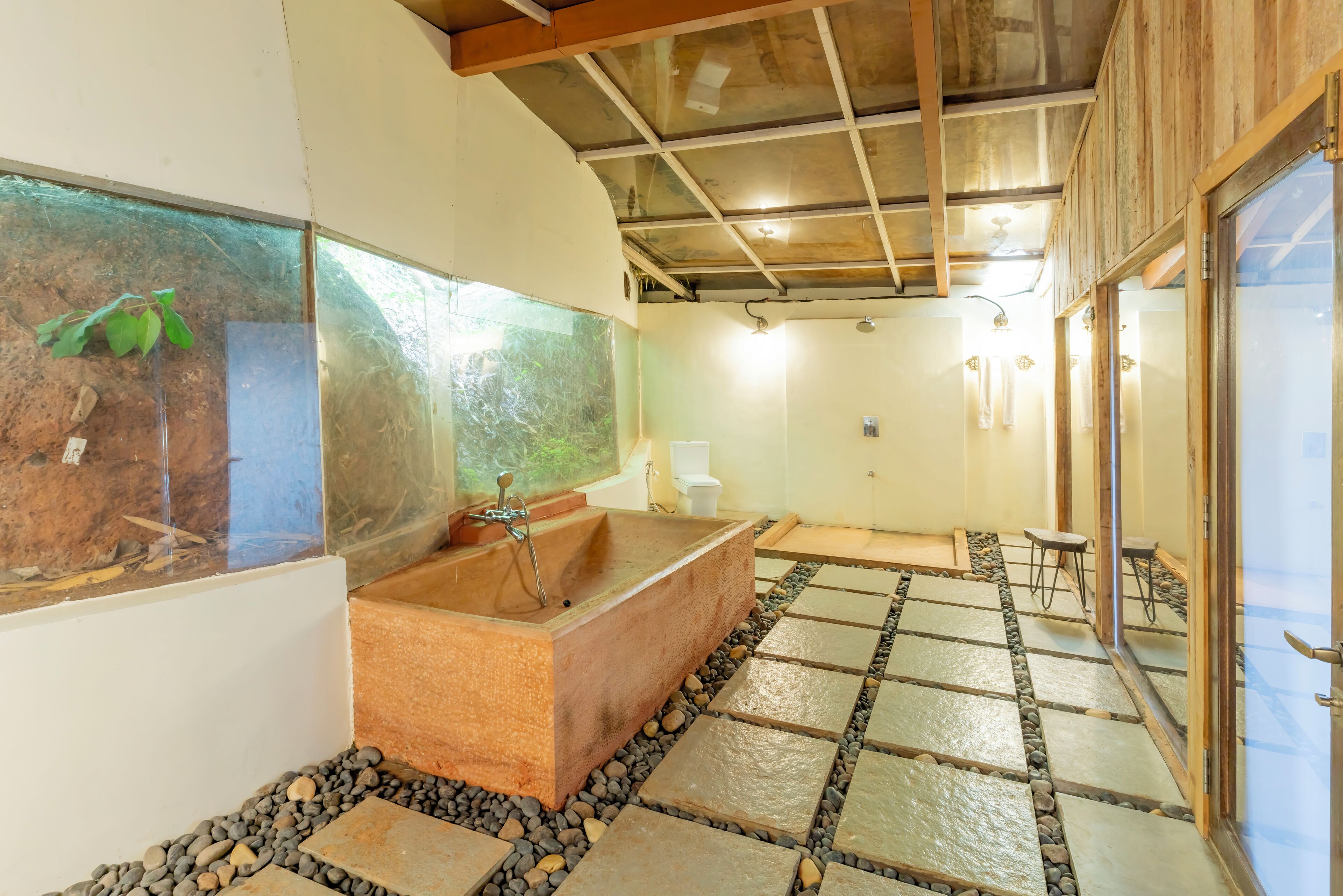 A bathroom with a large bathtub, a glass fish tank, and a stone-tiled floor.