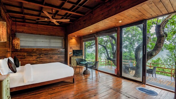 A wooden bedroom with a bed, a desk, and a large window overlooking a deck. - Forest Hills at Tala (Tala)