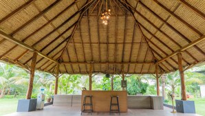 A covered outdoor area with a thatched roof, wooden beams, and a central hanging light fixture. - Forest Hills at Tala (Tala)