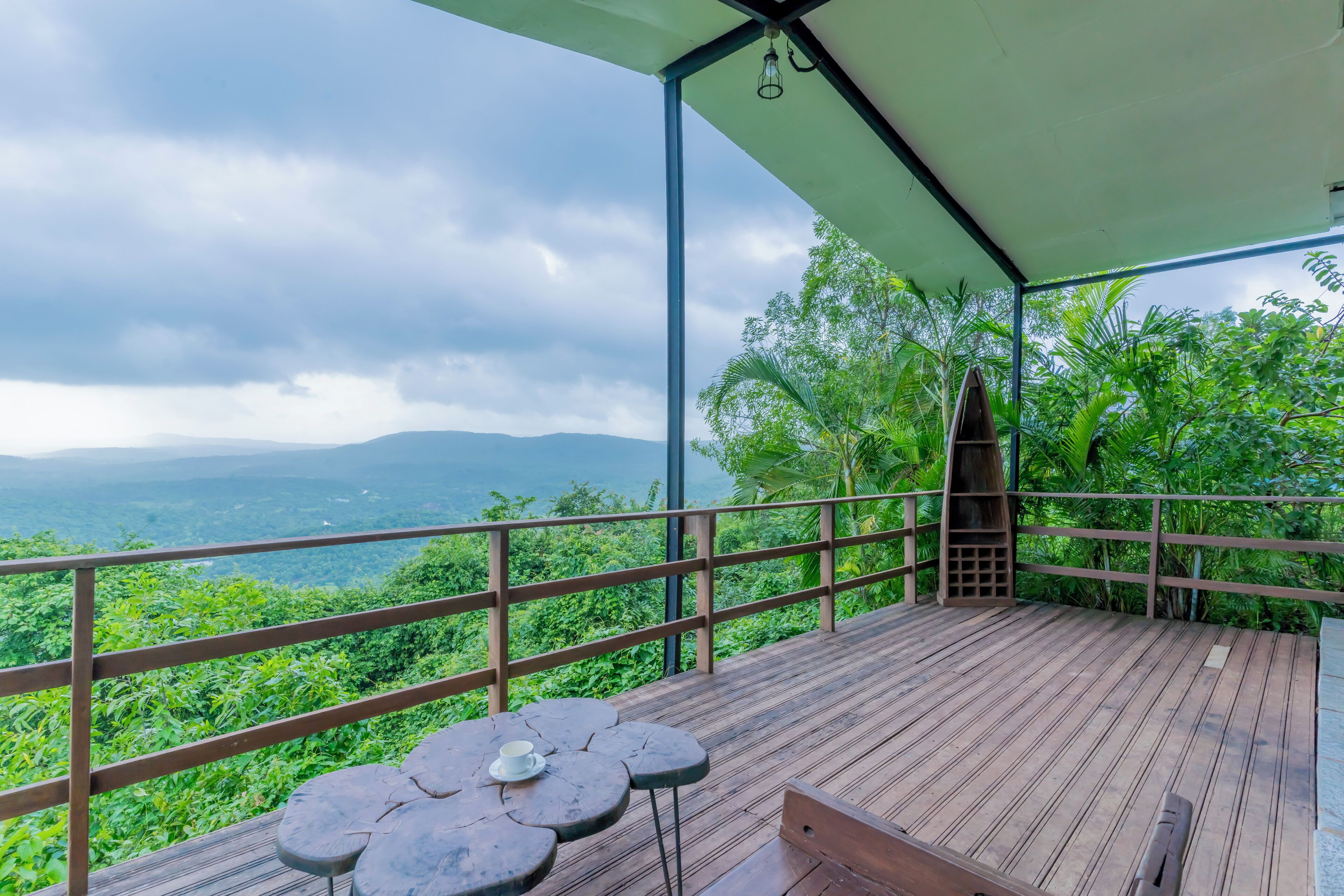 A wooden deck with a table and bench, overlooking lush greenery and distant mountains.